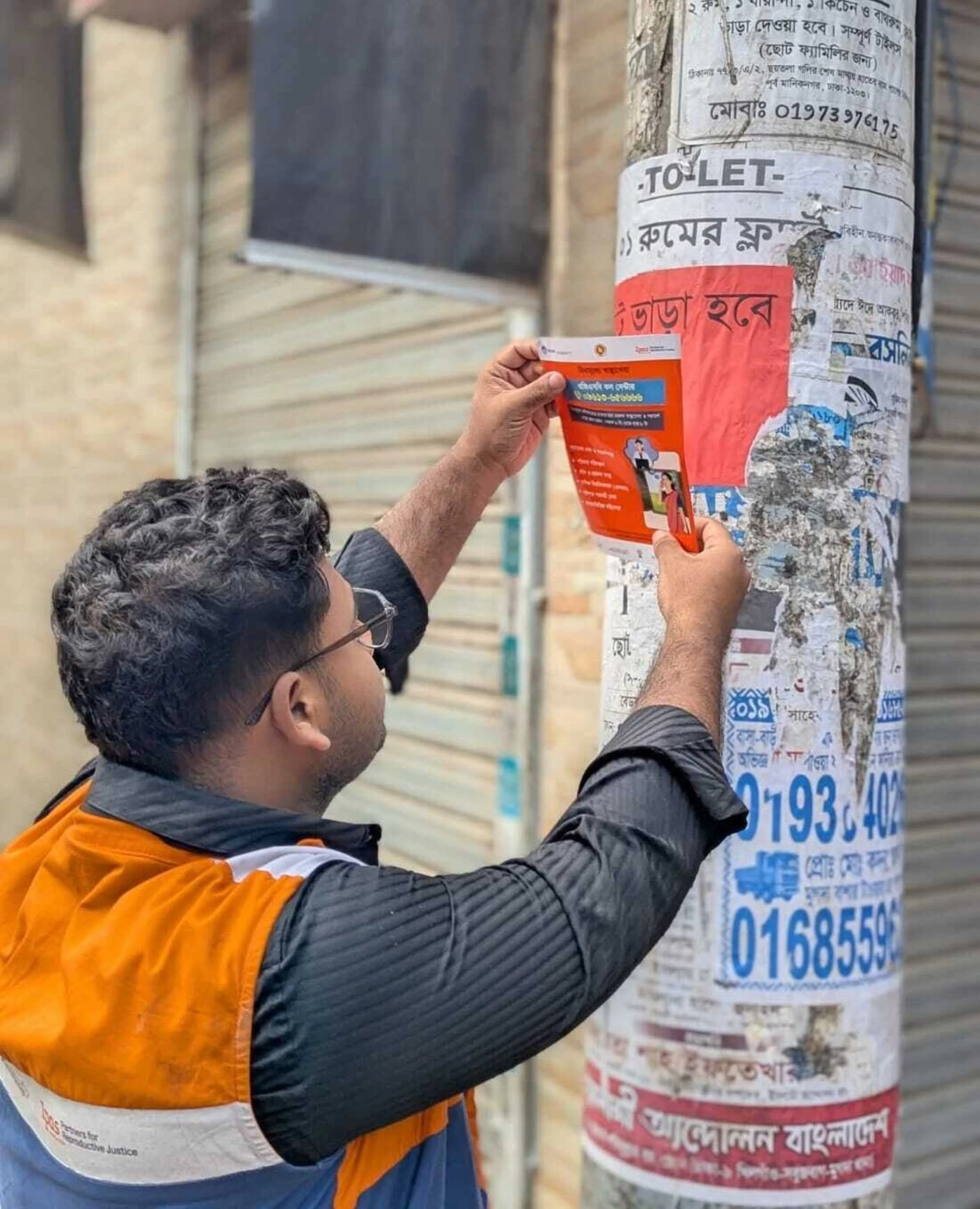 Abir is pasting a GP service related sticker on a roadside electric pole